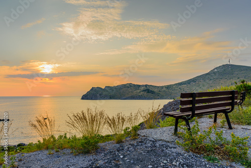 Fototapeta Naklejka Na Ścianę i Meble -  Beautiful sunset on the sea. Viewpoint with a bench on top of a hill. Skala village on Patmos island, Dodecanese, Greece.