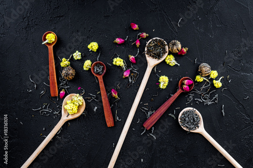 Aromatic tea. Wooden spoons with dried tea leaves, flowers and spices on black background top view