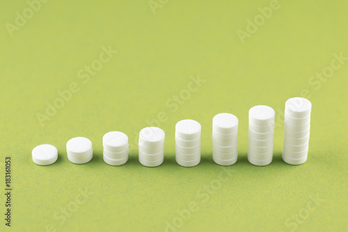 Close up pyramid concept of white pills on olive yellow background with copy space. Focus on foreground  soft bokeh. Pharmacy drugstore concept