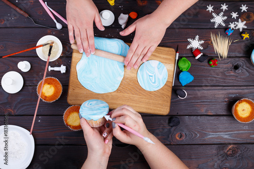Schilderij op canvas Friends rolling confectionery mastic and decorating cupcakes, view from above
