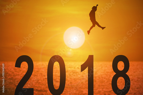 Silhouette of young man jumping over the numbers 2018 years with beautiful sunset at the sea, concepts of news year and business target.