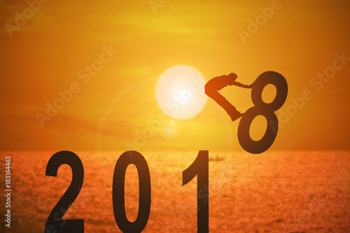 Silhouette of young man jumping over the numbers 2018 years with beautiful sunset at the sea, concepts of news year and business target.