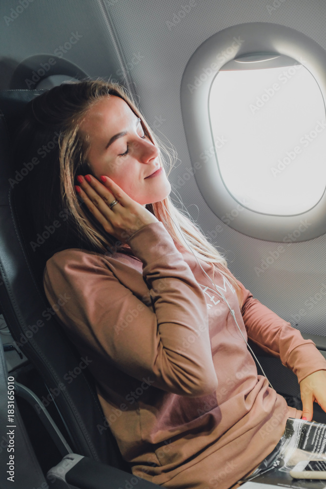 Girl near the window in airrplane listening music in headphones