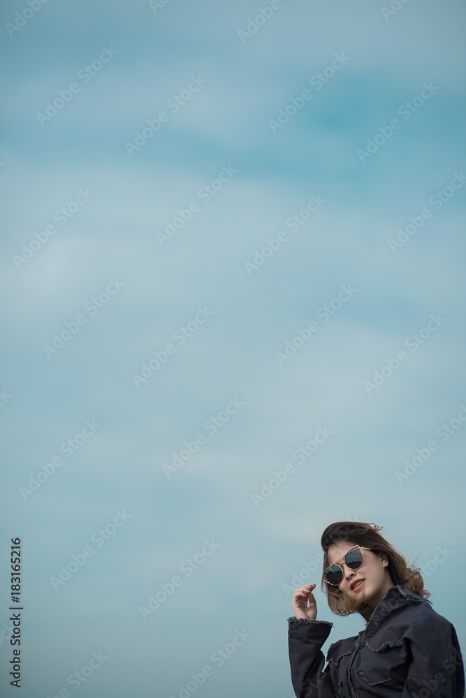 Portrait of asian girl short hair standing on a cliff behind the blue sky. Woman with sunglasses over sky background. Freedom concept.