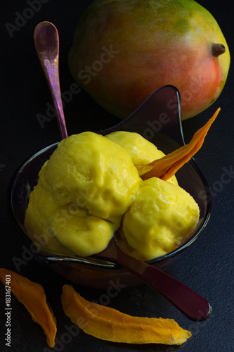 Mango-Eiscreme in Desserschale mit ganzer Mango im Hintergrund photo