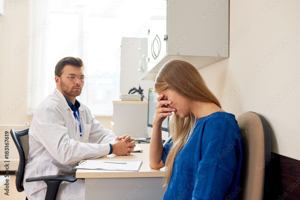 Fototapeta premium Portrait of sad young woman crying in doctors office consulting about serious illness, copy space