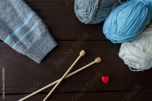 Knitting accessories: sleeve of knitted sweater, balls of yarn, needles for knitting and red heart symbolizing love to knitwear