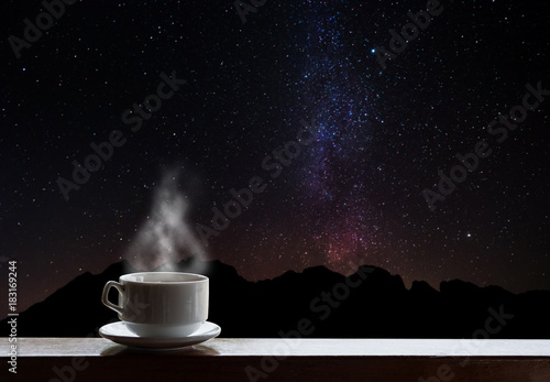 Cup of hot drinks on the table with beautiful Milky Way with silhouette mountain ride. Milky Way sightseeing at night © SasinParaksa