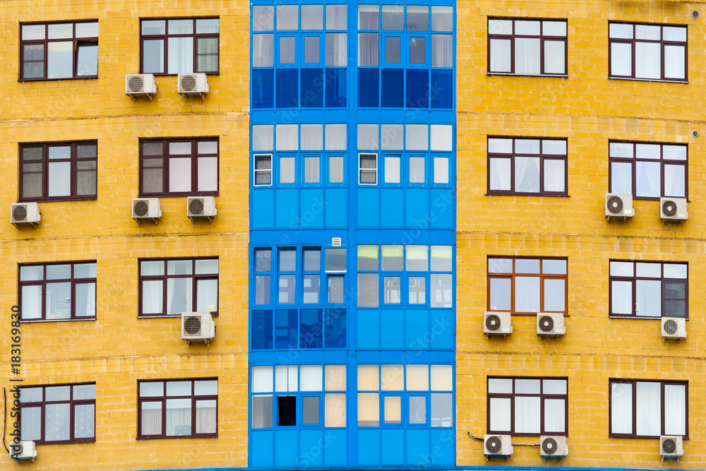 Yellow and blue facade of a modern residential building with air conditioning  (background, texture)