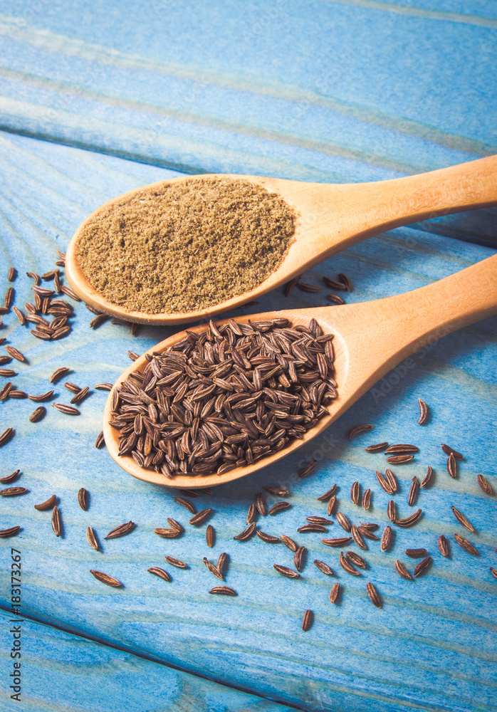 Ground cumin in a spoon and whole cumin on the wooden background. Ground cumin in a spoon and whole cumin on the wooden background.