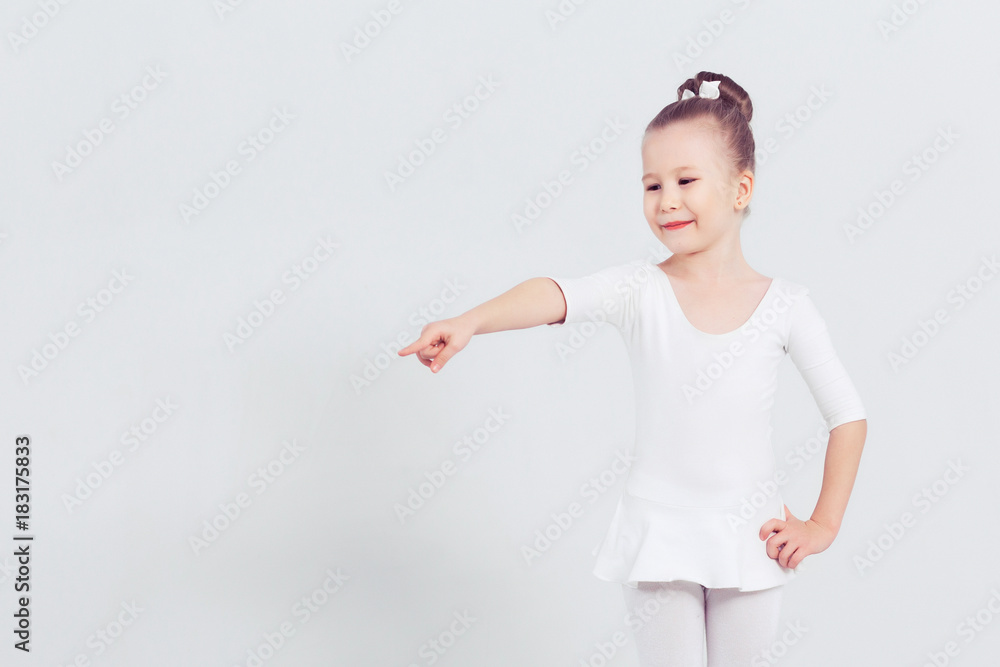 Little child girl dance ballet at white background. Portrait of small ballerina smiling and looking at camera, copy space Little child girl dance ballet at white background. Portrait of small ballerina smiling and looking at camera, copy space