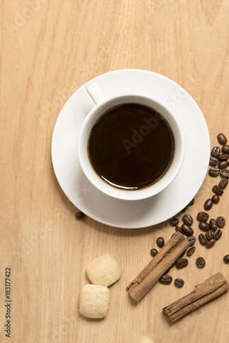 Black coffee in a cup and saucer with coffee beans, a cinnamon stick and biscuits on a wooden background 
