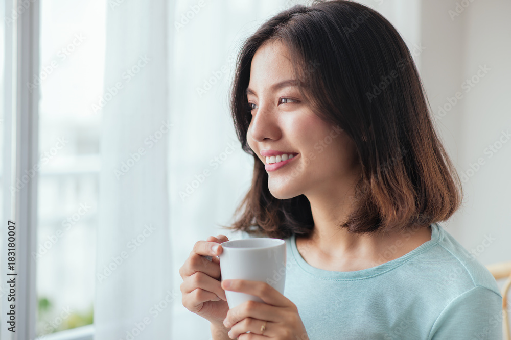 Smiling asian woman drinking coffee relaxing on the couch at home