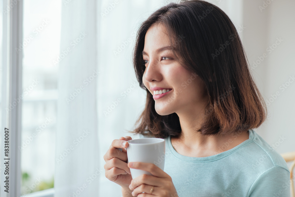 Smiling asian woman drinking coffee relaxing on the couch at home Smiling asian woman drinking coffee relaxing on the couch at home