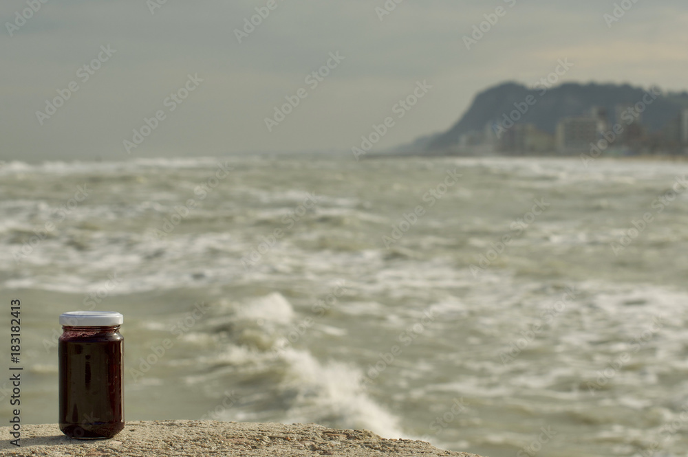 barattolo pieno con tappo bianco appoggiato su una scogliera con il mare in tempesta nel secondo piano barattolo pieno con tappo bianco appoggiato su una scogliera con il mare in tempesta nel secondo piano