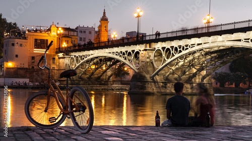 Evening scene couple and bike with background of Triana bridge, Seville