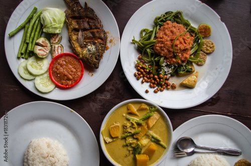 Indonesian food: Kankung plecing (spicy water spinach dish), Ikan goreng (fried fish) and kare (curry) top view. photo