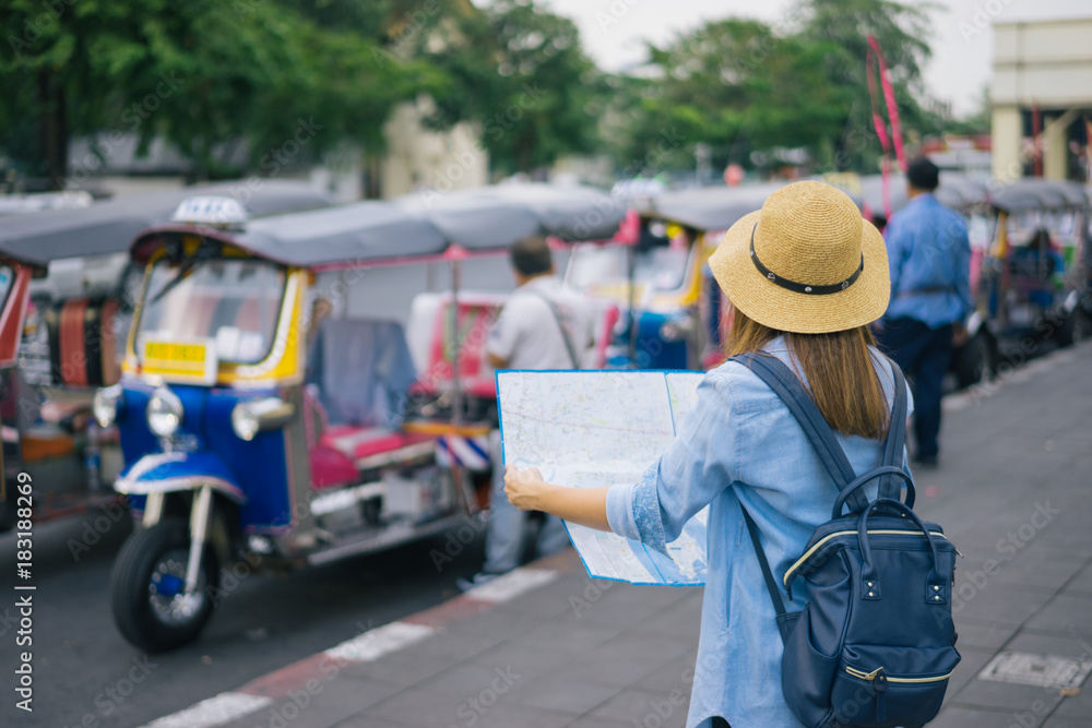 Young woman traveler with sky blue backpack and hat looking the map with tuk tuk Thailand background from china town Bangkok. Traveling in Bangkok Thailand. Travel concept