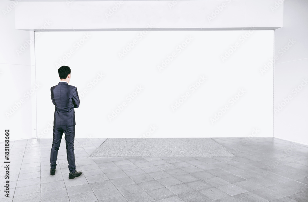 Businessman in black suit standing in empty interior with mock up white space Businessman in black suit standing in empty interior with mock up white space