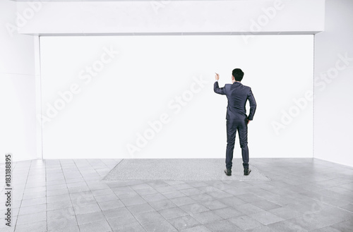 Businessman in black suit writing on empty interior with mock up white space