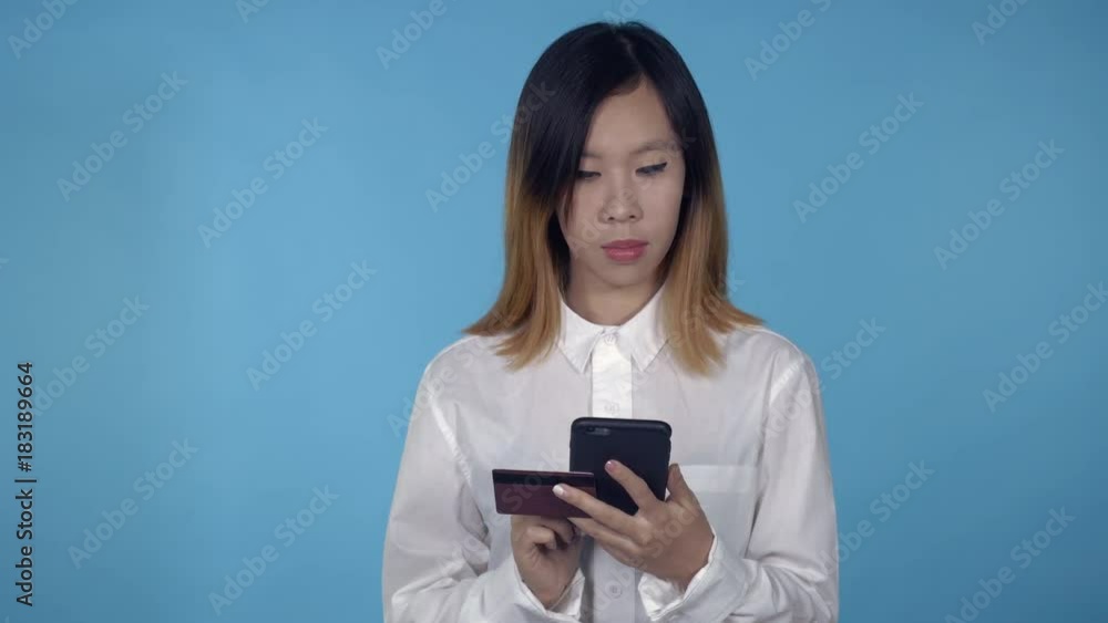 young asian woman using smartphone for buying online or pay order or bills on blue background in studio. attractive millennial girl wearing white casual shirt looking at the camera smiling young asian woman using smartphone for buying online or pay order or bills on blue background in studio. attractive millennial girl wearing white casual shirt looking at the camera smiling