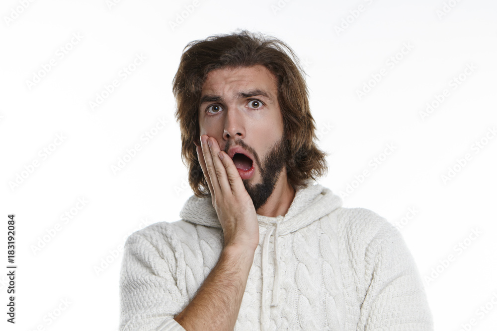 Shock, surprise and astonishment concept. Picture of surprised young male with fuzzy beard and voluminous hair opening mouth widely and holding hand on his cheek, shocked with intriguing gossip Shock, surprise and astonishment concept. Picture of surprised young male with fuzzy beard and voluminous hair opening mouth widely and holding hand on his cheek, shocked with intriguing gossip