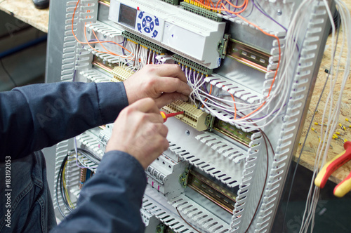 Technician assembling low voltage assembling industrial HVAC control panel in workshop. Close-up photo of the hands.