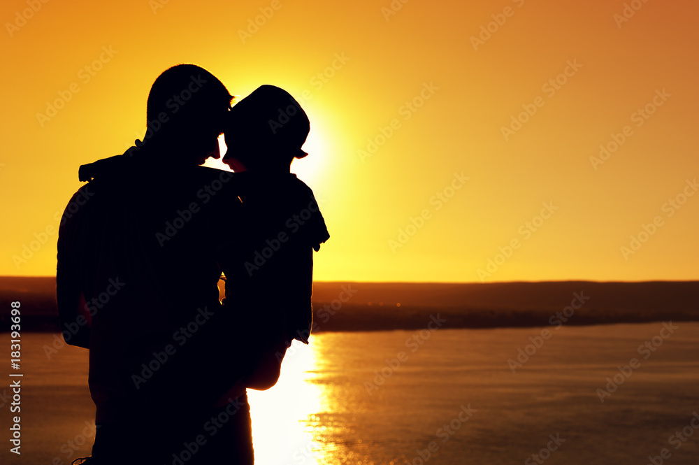 Rear view - silhouette of the father holding his little son in arms and admiring the sea view on sunny summer evening