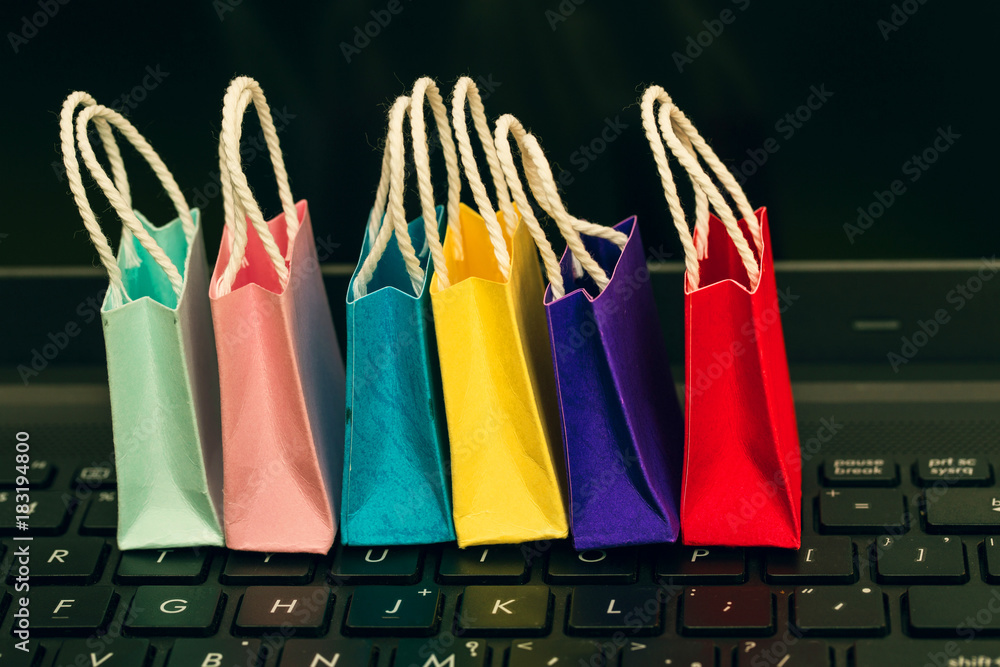 Row colorful paper shopping bags with mobile phone on a laptop keyboard. Ideas about online shopping or shopping at home or office which customers can purchase items or services or goods remotely.