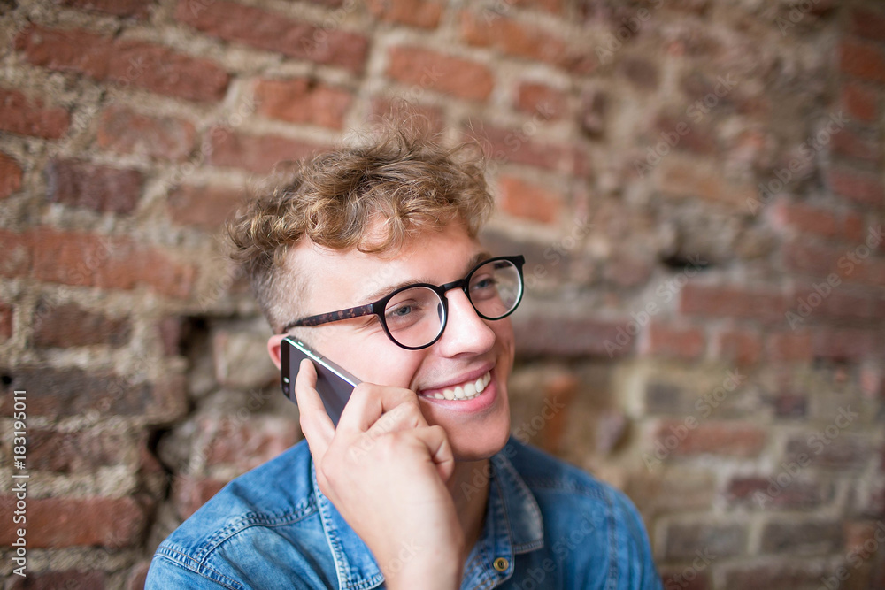 Young smiling hipster guy talking on portable mobile phone. Handsome happy man having pleasant cell telephone conversation. Stylish cheerful male using modern cellphone during free time Young smiling hipster guy talking on portable mobile phone. Handsome happy man having pleasant cell telephone conversation. Stylish cheerful male using modern cellphone during free time