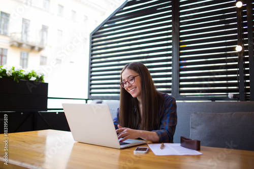 Young happy businesswoman having on-line conference on laptop computer during rest in restaurant. Smiling female manager having video call on net-book. Hipster girl using notebook. Copy space