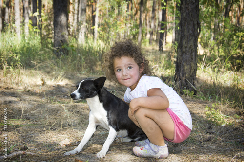 In the summer in the forest a little girl hugs a dog