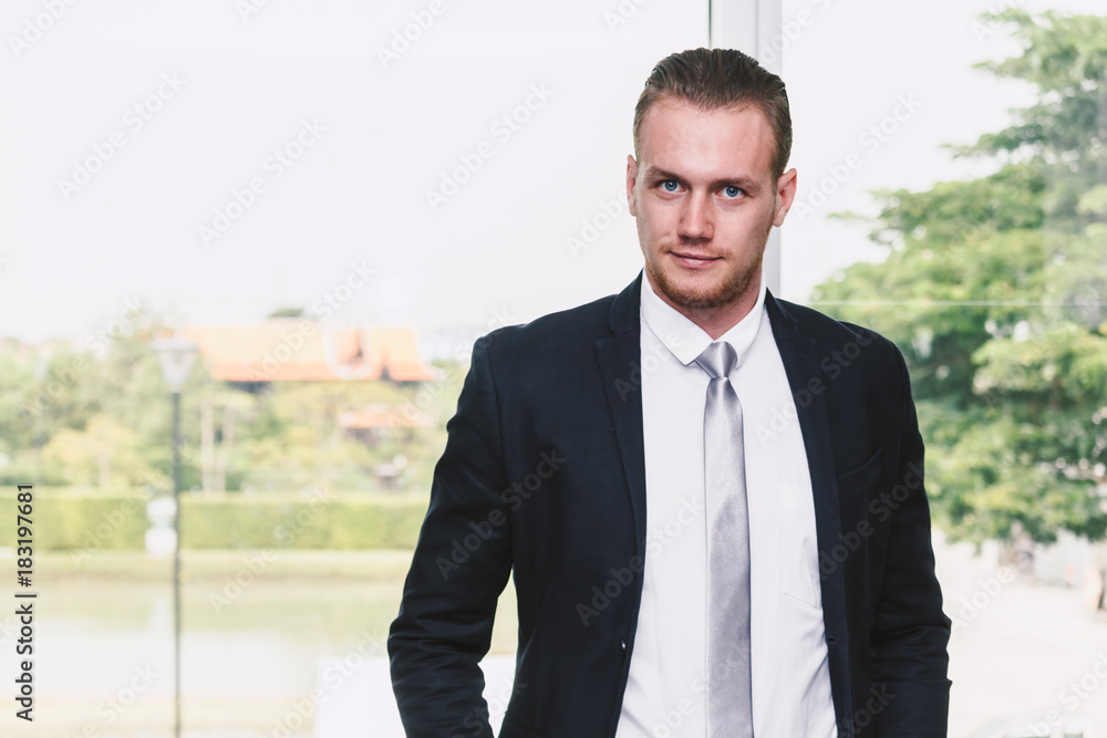 Portrait of handsome man in black suit standing in office Portrait of handsome man in black suit standing in office