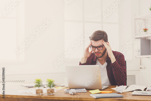 Young stressed businessman with laptop in modern white office