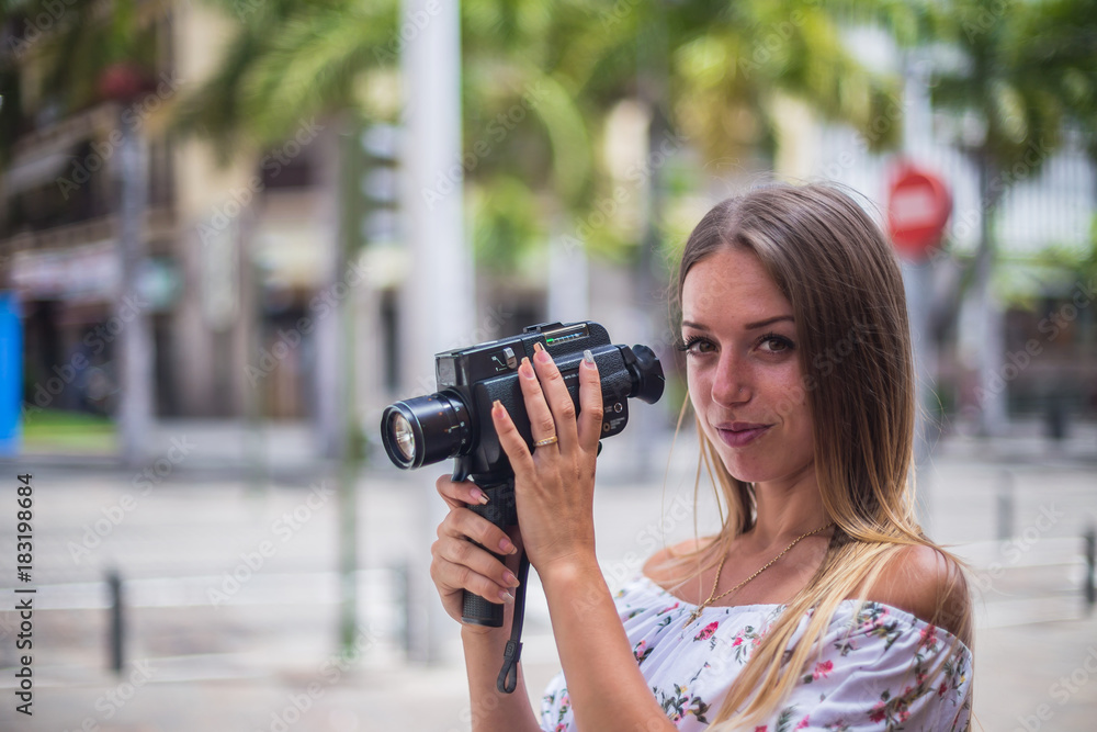 Tenerife. Spain. Cute blonde girl is observing and filming streets in Santa Cruz de Tenerife. Girl travels concept. Travel to Canary Islands. Tenerife. Spain. Cute blonde girl is observing and filming streets in Santa Cruz de Tenerife. Girl travels concept. Travel to Canary Islands.