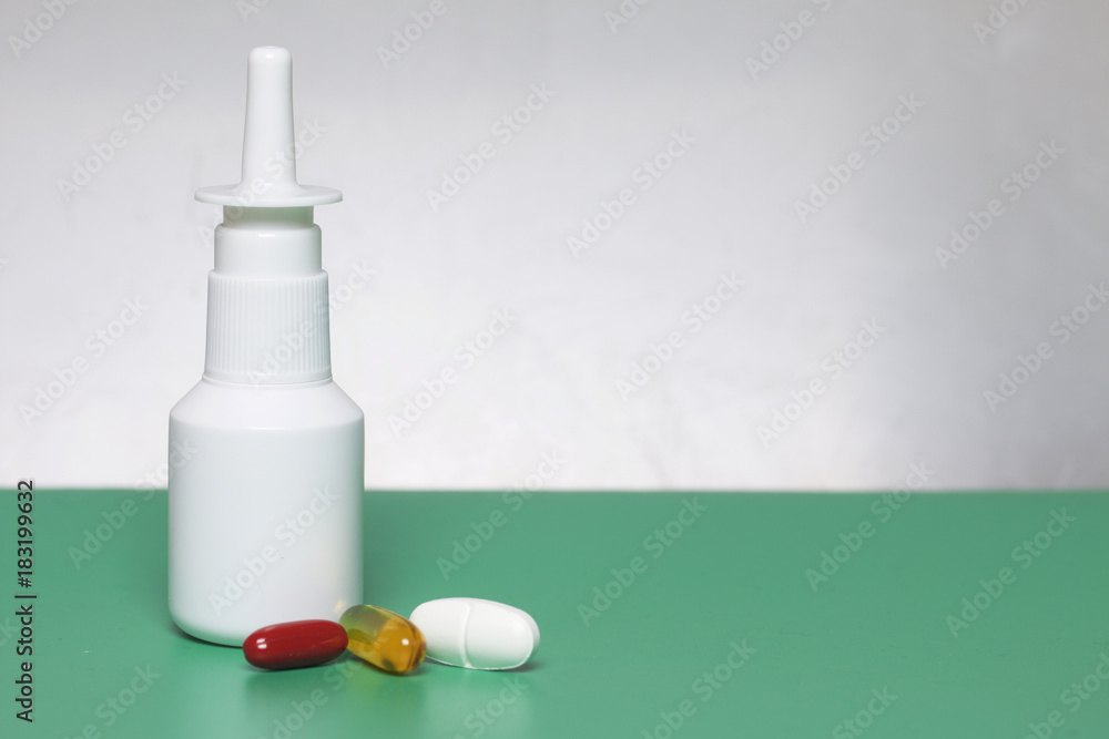 Nasal stand on the surface. On a surface of green color, on a white background. Nearby lie medical pills of different colors. Nasal stand on the surface. On a surface of green color, on a white background. Nearby lie medical pills of different colors.