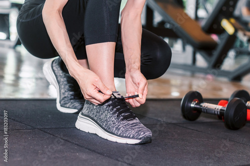 Woman tying her shoelaces with fitness equipment in the gym