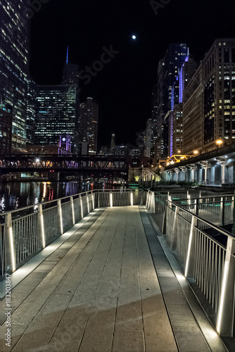 Chicago city riverwalk promenade at night with vintage drawbridge, illuminated urban downtown buildings and the moon.