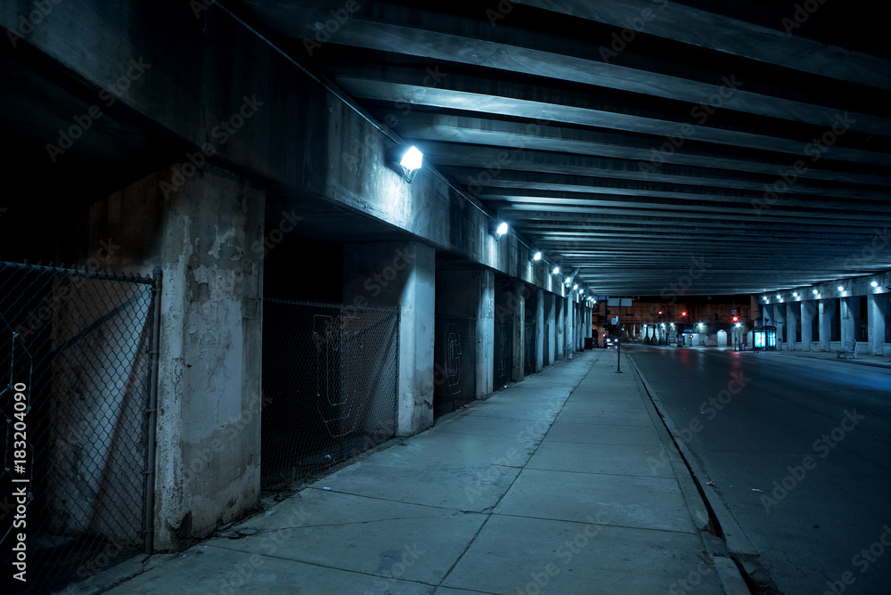 Gritty dark Chicago city street with industrial train bridge viaduct tunnel at night.