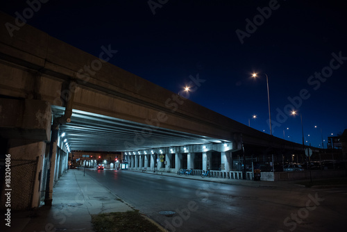 Gritty dark Chicago highway bridge and city street with a car and bicycle stand at night. © Bruno Passigatti