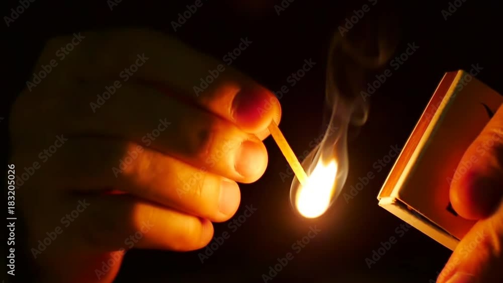 Man lights up a machstick with the matchbox in the darkness. Slow