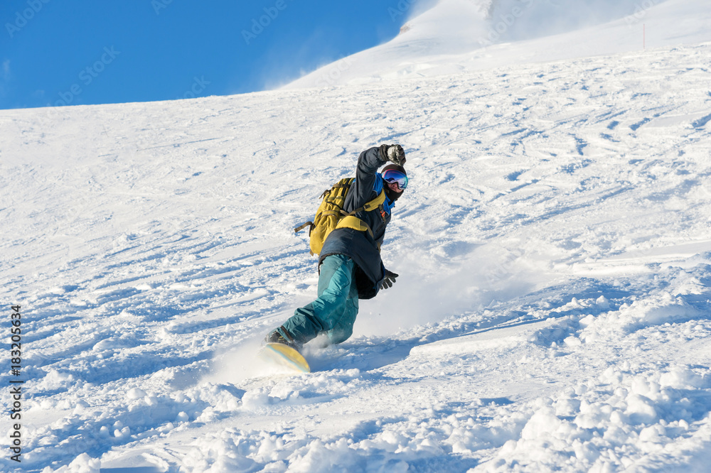 Freeride snowboarder rolls on a snow-covered slope leaving behind a snow powder against the blue sky Freeride snowboarder rolls on a snow-covered slope leaving behind a snow powder against the blue sky