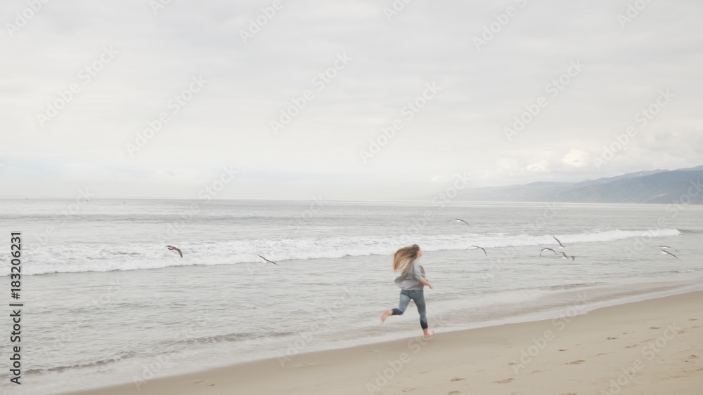 teen girl running on Santa Monica beach in cloudy november day motion blur