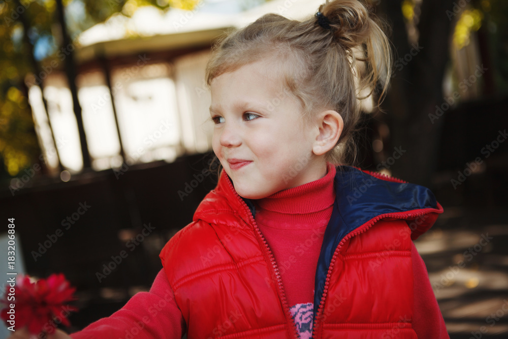 Cute girl blonde in a red jacket holding a flower in the Park outdoors Cute girl blonde in a red jacket holding a flower in the Park outdoors