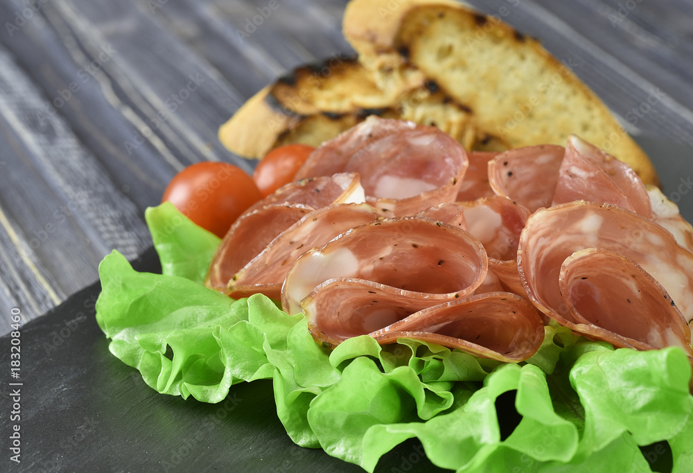 cold meat plate. Sliced ham with lettuce leaves on a dark stone background, selective focus cold meat plate. Sliced ham with lettuce leaves on a dark stone background, selective focus