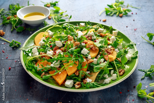 Fresh Tasty Persimmon salad with arugula, nuts, feta cheese, olive oil and herbs. healthy food