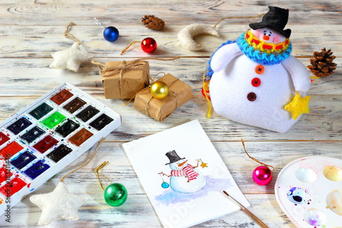 New Year (Christmas) cards with funny snowman and toy textile snowman on white boards background with watercolors, brush, gist box, toy stars and moon. Merry christmas and happy new year greeting card