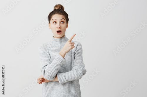 Teenage girl with wonder looking to side and showing with index finger. Curious female employee trying to pay attention over white background. Attention concept