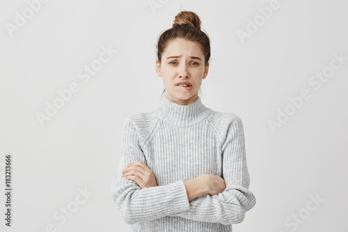Puzzled woman wearing casual clothes standing with arms crossed looking at camera. Female illustrator biting lips with feelings of regrets about work. Emotions concept