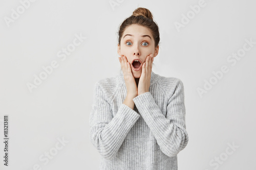 Attractive woman looking on camera with open mouth being shocked. Female student grabbing face being astonished about exam result. Education concept